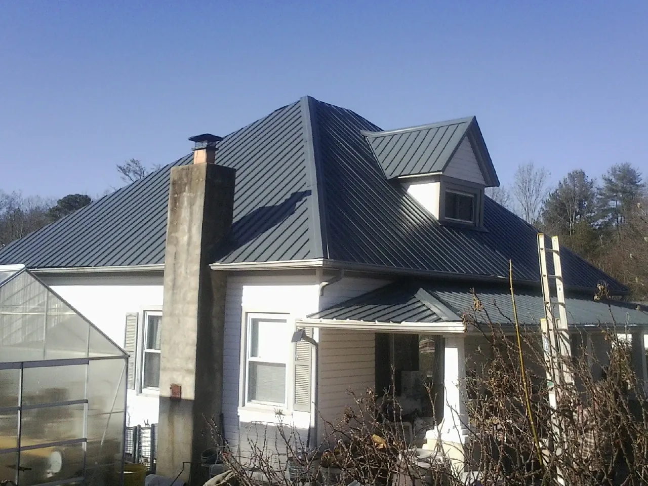 Dark blue standing seam metal roof on a white farmhouse with dormer — Slate & Tile Roof Repair by Roofing Brothers in Taberg