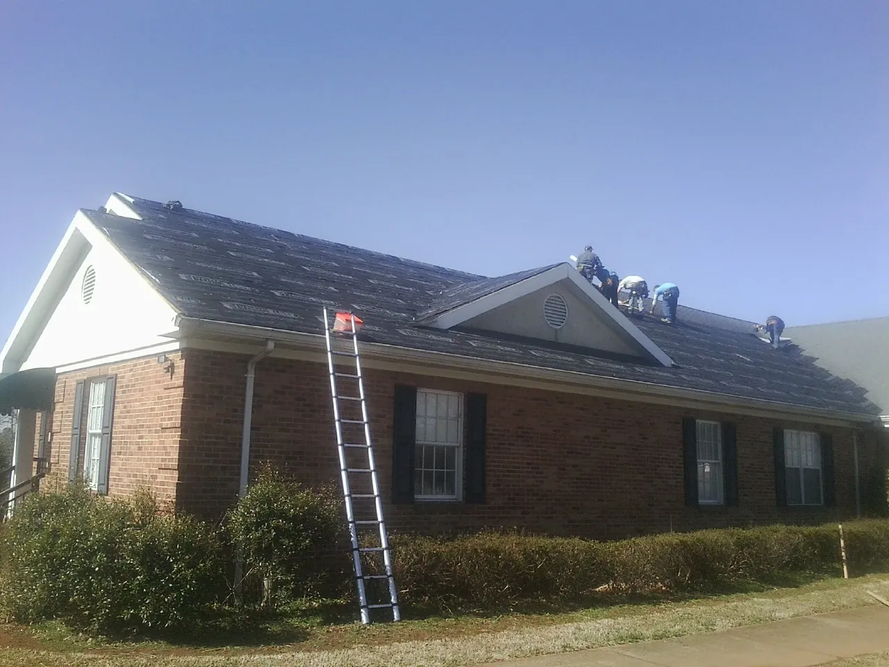 Crew tearing shingles off a brick ranch roof with a ladder set — Metal Roof Repair work by our crew in Taberg
