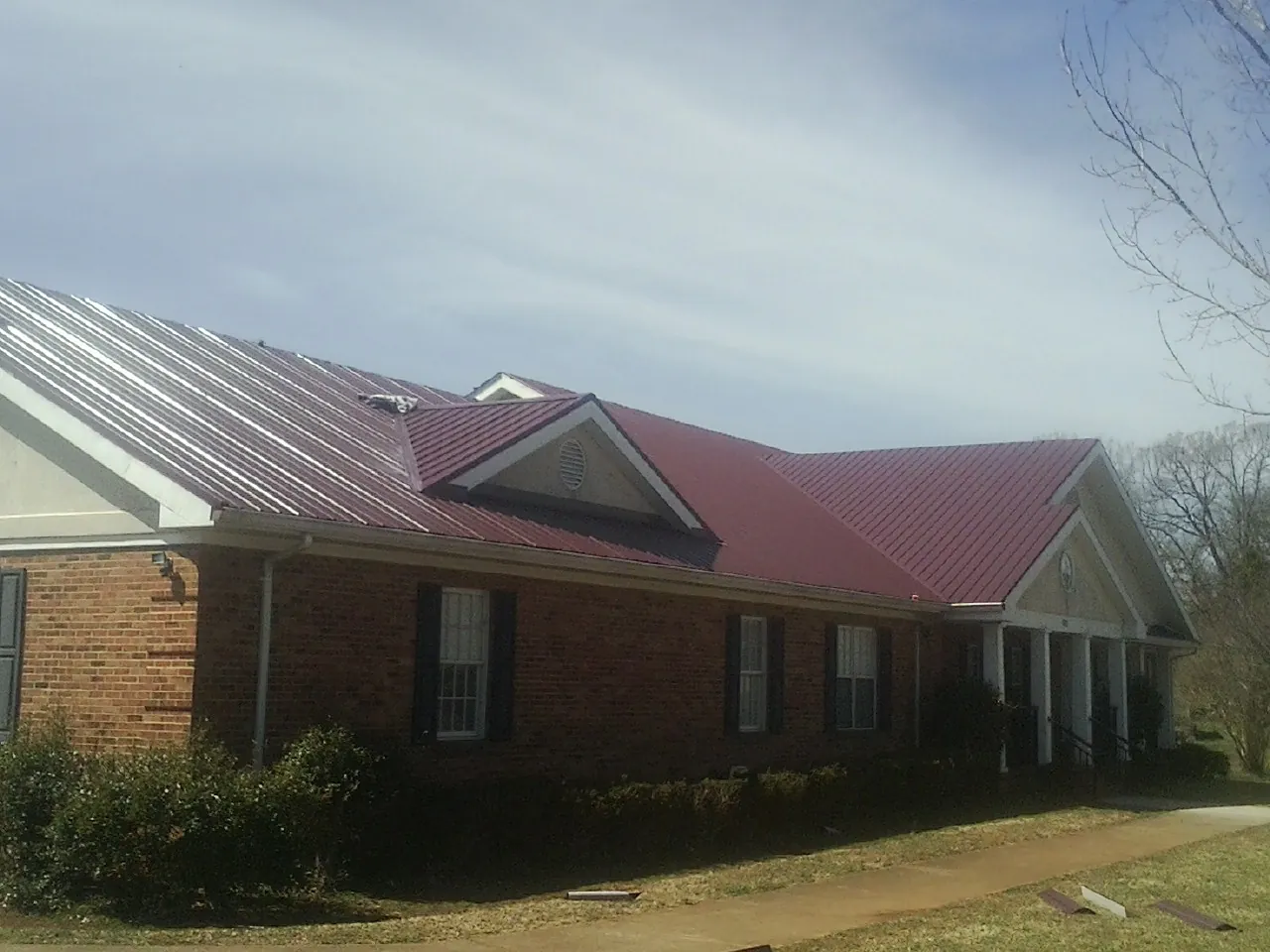 Red metal roof with gabled entries on a long brick building, from a Hail Damage Roof Repair job in Taberg