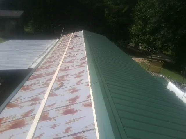 Old rusted panels beside newly installed green metal roofing — Wind Damage Roof Repair by Roofing Brothers in Taberg