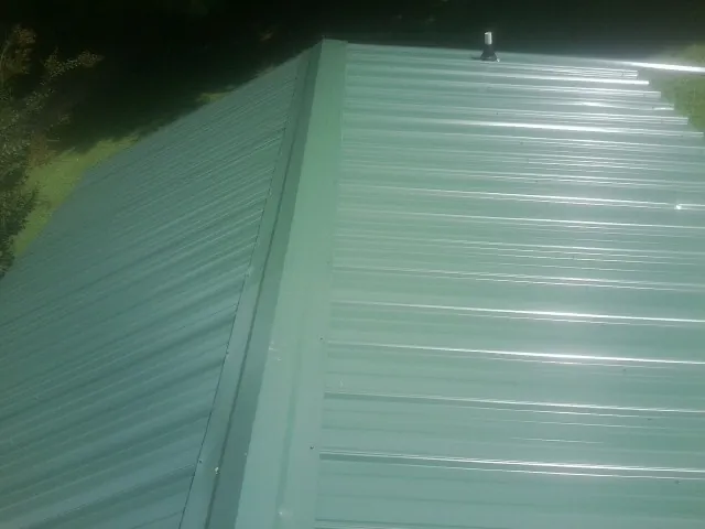 New green metal panels meeting at the ridge of a roof — Flat Roof Repair work by our crew in Taberg