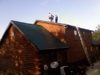 Crew on the ridge of a green metal roof on a two story log home in Taberg