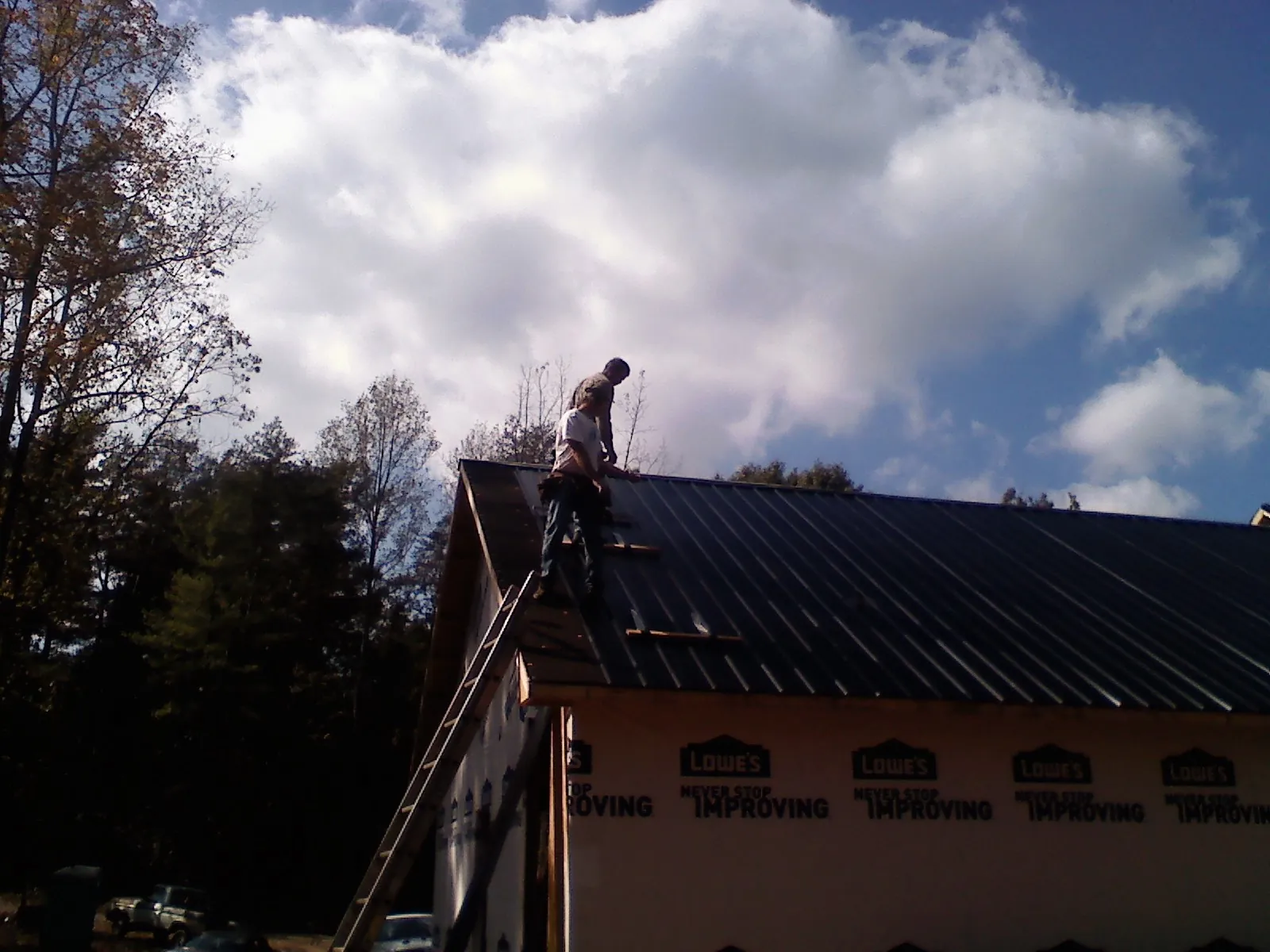 Roofer fastening dark metal panels high against a cloudy sky, from a Roof Inspection job in Taberg