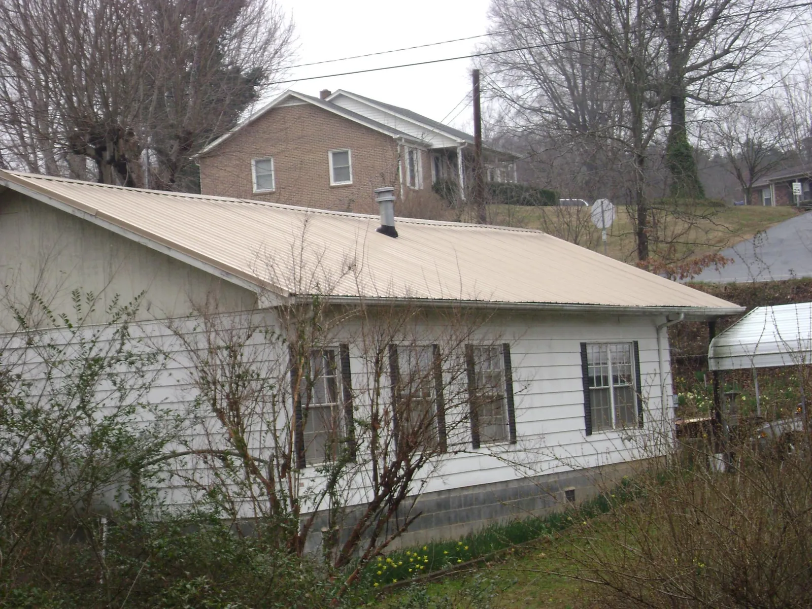 Tan metal roof on a white sided house set into a hillside — Commercial Roofing by Roofing Brothers in Taberg