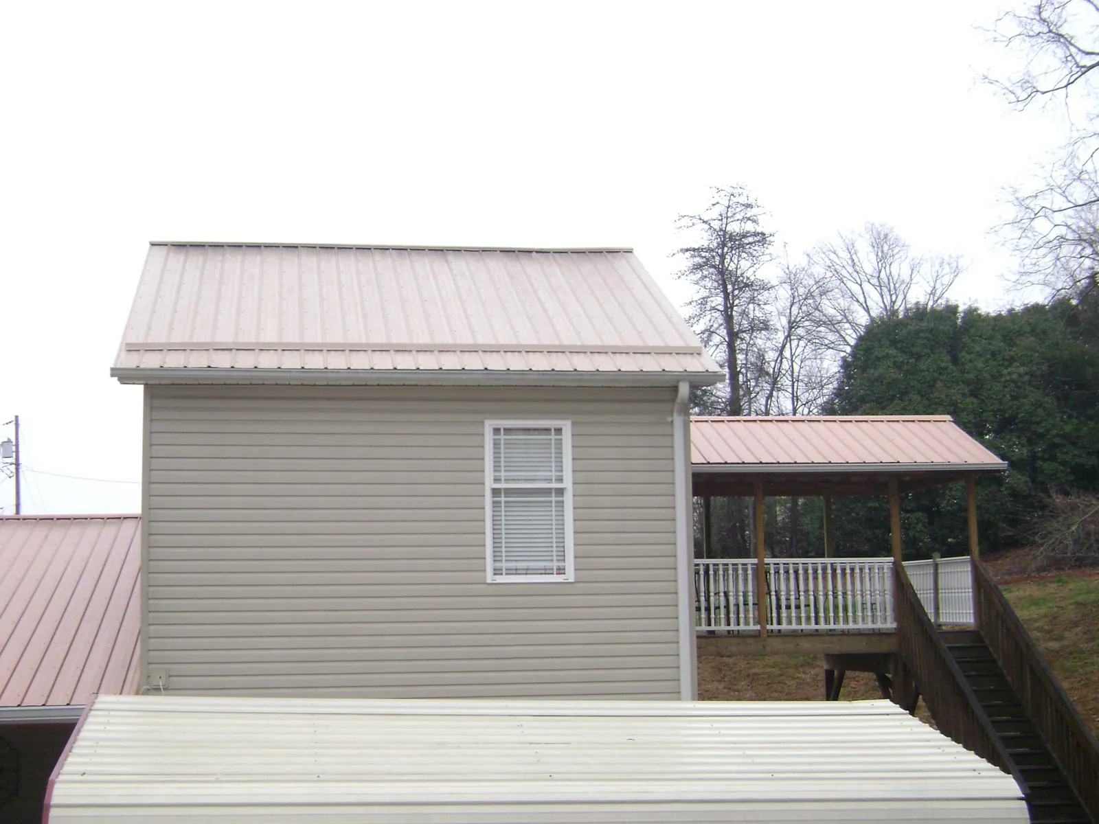 Tan metal roofs on a two story addition and attached porch, from a Roof Replacement job in Taberg
